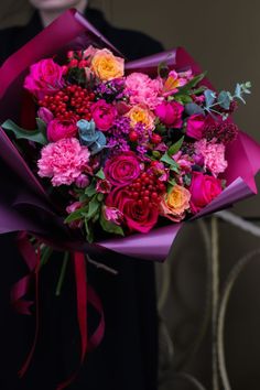 a woman holding a bouquet of flowers in her hands and wearing a black dress with red ribbon