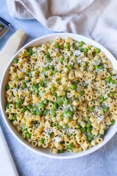 a bowl filled with pasta and peas on top of a blue table cloth next to a knife