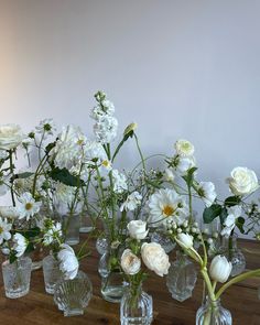 there are many glass vases with flowers in them on the wooden table next to each other