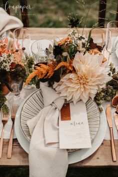 the table is set with white plates and silverware, orange flowers, and greenery