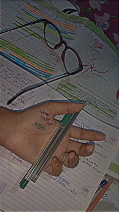 a person's hand holding a pencil and pointing at papers with writing on them