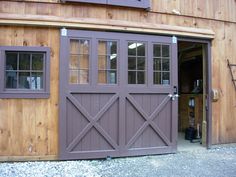 an open garage door in front of a wooden building with windows on each side and doors to the other side