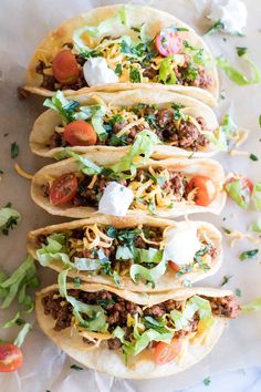 four tacos with meat, lettuce and tomatoes