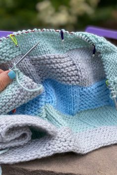 someone is knitting something with needles on top of the blanket and another item in the background