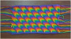 a multicolored crocheted blanket with fringes on it sitting on a wooden surface