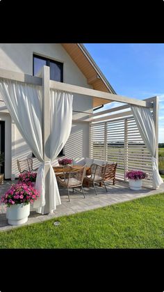 a patio covered in white curtains next to a table with chairs and potted flowers