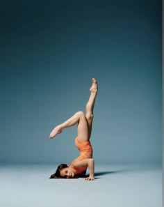 a woman in an orange leotard doing a handstand on the floor