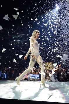 a woman in white outfit walking on stage with confetti falling from the sky