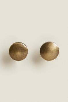 two brass - plated earrings on a white surface, one is round and the other is oval