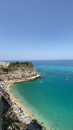 the beach is crowded with people and boats in the blue water near an old city