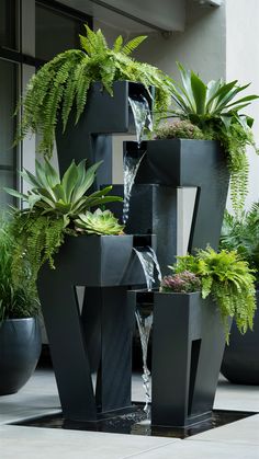 several black planters with plants and water running down them in front of a building