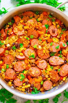 a large pot filled with sausage, corn and rice next to cilantro leaves