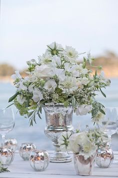 a vase filled with white flowers sitting on top of a table next to wine glasses