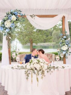 a bride and groom kissing in front of a table with flowers on it at their wedding reception