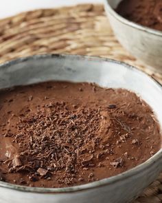 two metal bowls filled with chocolate pudding on top of a woven place mat next to each other