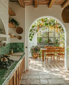 an arched doorway leads into a kitchen with green tile and wood furniture, along with potted plants on the counter