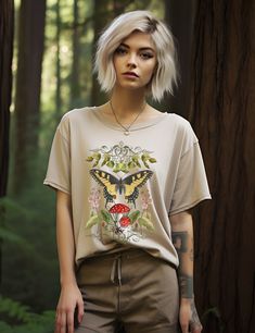 Get 10% off your first order: join.lucidamystica.com Vintage-style dark cottagecore collage with butterfly, flowers and mushrooms on a super-soft modern-fit unisex tshirt. Easily bring the cottagecore/nature aesthetic into your everyday wardrobe.  Comes in 2 colorways: Natural and Dark Olive Green.  Plus sizes available for a roomy fit. Size up for an oversized aesthetic look. Size chart found in images.  + Printed on Bella + Canvas 3001 unisex tshirt + Retail fit + 100% Soft cotton  + Light fab Summer Fairycore Top With Graphic Print, Spring Mushroom Print Relaxed Fit Top, Bohemian Cotton Tops With Butterfly Print, Plus Size Goblincore, Fairy Grunge Clothing, Grunge Clothing Aesthetic, Cottagecore Collage, Goblincore Clothes, Cottagecore Butterfly