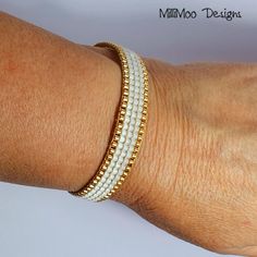 a woman's arm wearing a bracelet with white beads and gold chains on it