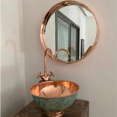 a bathroom sink sitting under a mirror next to a wooden table with a metal bowl on it