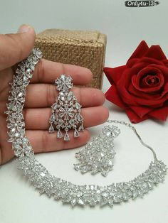 a hand holding a necklace and earrings next to a rose