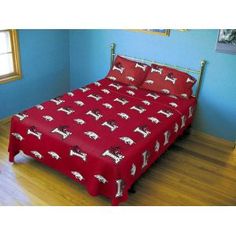 a bed in a room with blue walls and wooden floors, has a red bedspread with white dogs on it