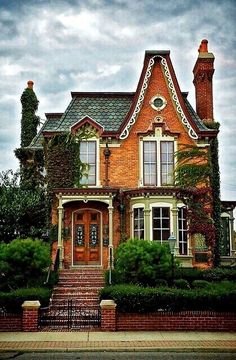 a large brick house with lots of windows and bushes on the front lawn, along with steps leading up to it