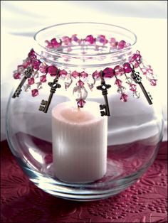 a candle is sitting in a glass bowl with pink beads and keys on the handle