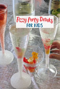 three champagne flutes filled with colorful liquid and sprinkles on top of a table