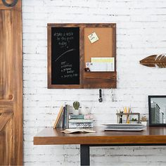 a wooden desk topped with a laptop computer next to a chalkboard wall mounted on a white brick wall