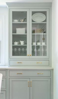 a gray china cabinet with glass doors and gold handles in a white dining room setting