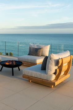 a couch and table sitting on top of a patio next to the ocean in front of a glass wall