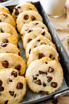 chocolate chip cookies are lined up in a baking pan next to a glass of milk