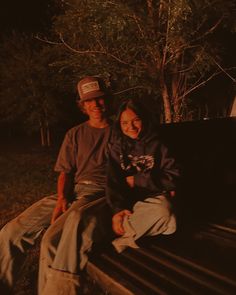 two people are sitting on a bench in the dark, one is wearing a hat