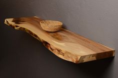 a wooden shelf with a small bowl on it's top, against a gray wall