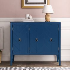 a blue cabinet with two doors and a lamp on top of it in front of a pink wall