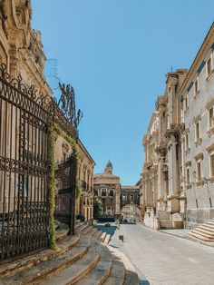 an old city street with stone buildings and wrought iron gates on both sides, surrounded by greenery