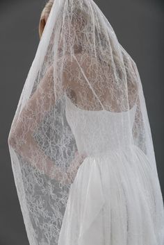 a woman in a white wedding dress with a veil on her head and hands behind her back