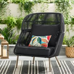 a black wicker chair sitting on top of a rug next to a potted plant