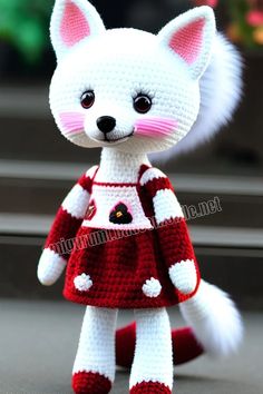 a crocheted white cat wearing a red and white dress