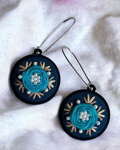 two pairs of earrings with blue and white flowers on them sitting on top of a blanket