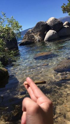 someone is holding their finger up to the water's edge with rocks in the background