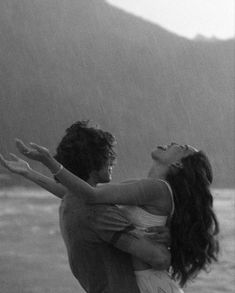 a man and woman are hugging in the rain by the ocean with their arms around each other