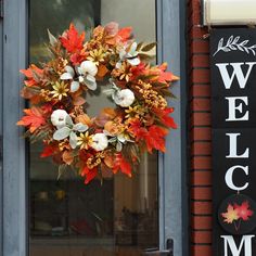 a wreath is hanging on the front door of a building with autumn leaves and pumpkins