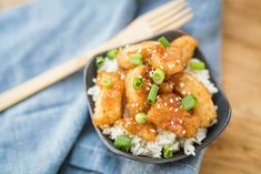 a black bowl filled with rice and chicken on top of a blue napkin next to chopsticks