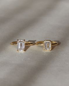 two gold rings with an emerald cut diamond