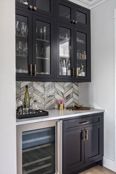 a kitchen with black cabinets and marble counter tops, wine glasses on the glass doors