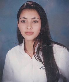 a woman with long dark hair wearing a white shirt and posing for a photo in front of a blue background