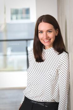 a woman standing next to a wall wearing a white and black polka dot shirt with her hands in her pockets