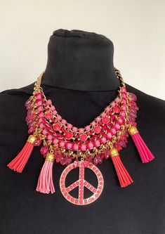 Fab, pink bead and piece charm statement necklace from Olivia Divine. Chunky, gold tone necklace with pink bead detailing. Large pink peace charm and tassel drop detailing. Adjustable length. Perfect for summer holidays, festivals, and nights our. Handmade and unique design. Pink Necklace For Summer Festivals, Pink Hippie Jewelry For Summer, Pink Bohemian Necklace For Party, Pink Hippie Style Summer Jewelry, Pink Hippie Jewelry For Festivals, Bohemian Pink Adjustable Charm Necklaces, Pink Bohemian Beaded Dangle Necklaces, Bohemian Pink Beaded Dangle Necklaces, Pink Bohemian Beaded Necklace For Party