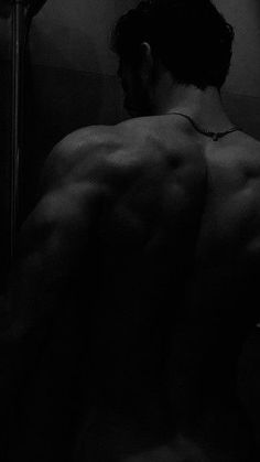 a man with no shirt is standing in front of a mirror and looking at his back